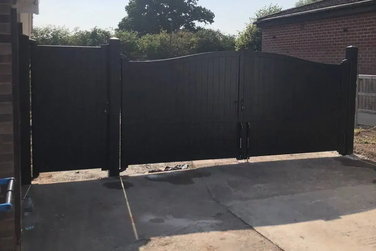 Black archtop aluminium driveway gates between brick houses