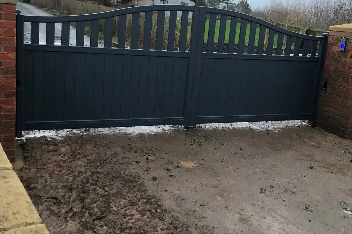 Dark grey arched aluminium swing gates between brick piers