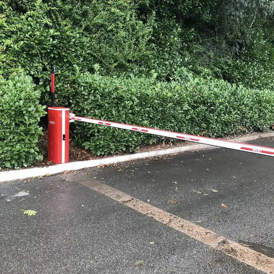 Red barrier with its arm lowered across a road beside a tall hedge