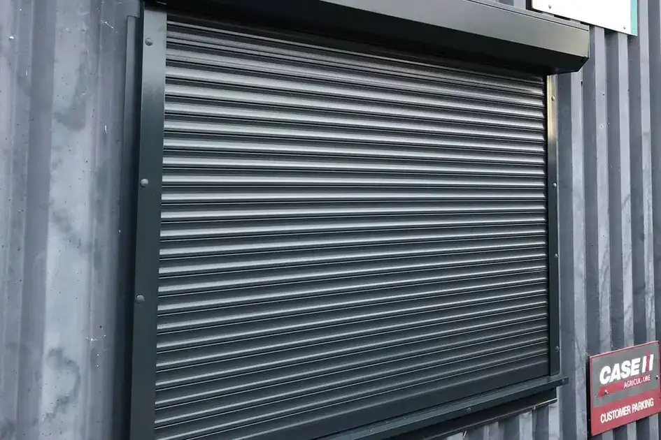 Dark grey roller shutter over a window on a corrugated steel building