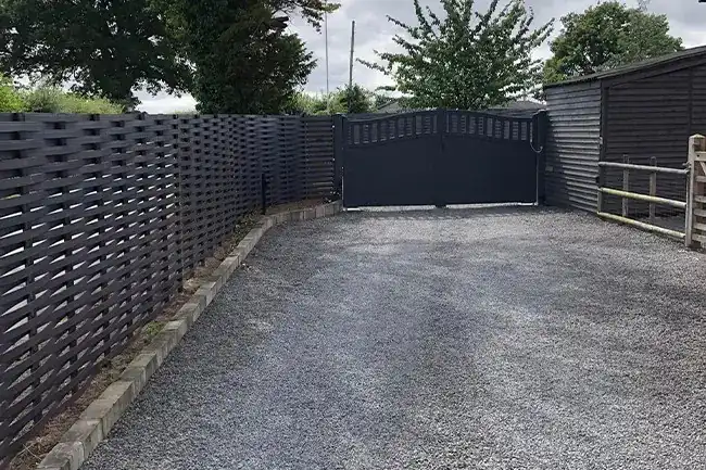 Dark grey woven steel fencing down both sides of a gravel drive to matching arched double gates