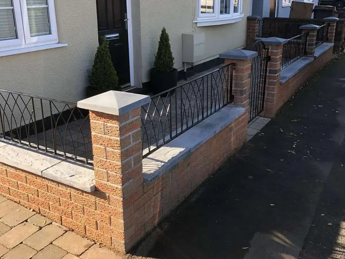 Black arched railings on low brick walls in front of a row of cream houses