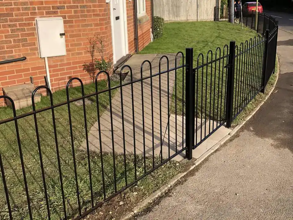 Black bow-top railings along a lawn beside a pavement, brick house behind