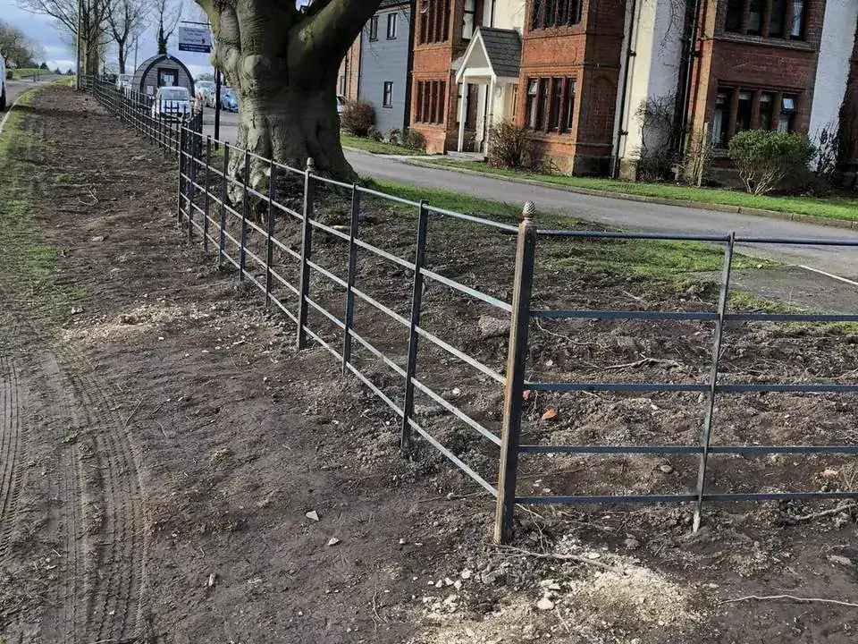New metal estate fencing along a verge under mature trees, houses beyond