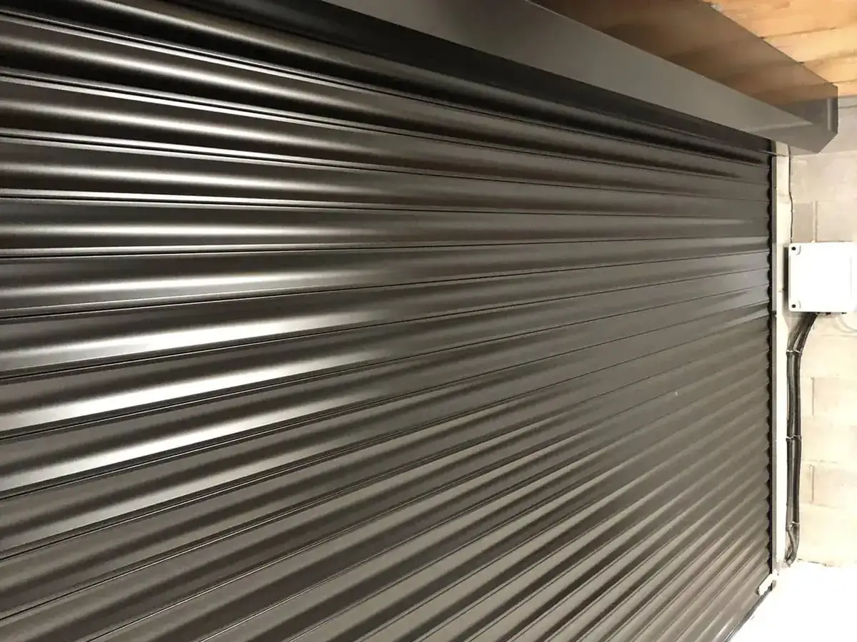 Black roller shutter closed across a wide opening under a timber-framed roof