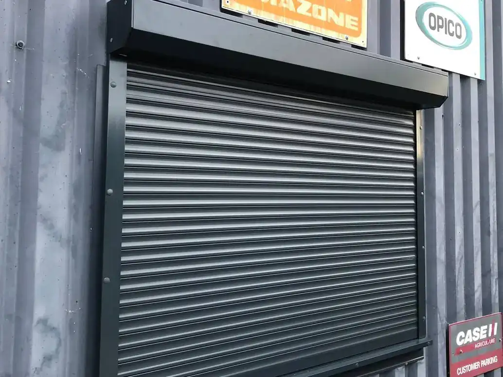 Dark grey roller shutter with its housing over a window on a corrugated steel building