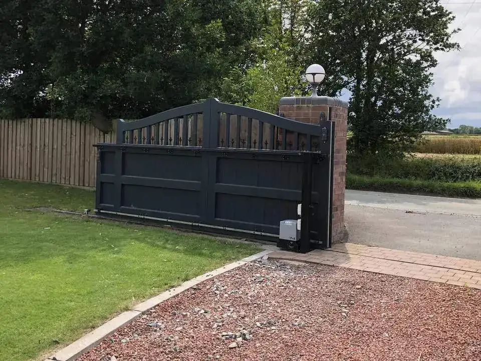 Anthracite arched gate between a fence and a brick pier, lawn and a red gravel drive in front