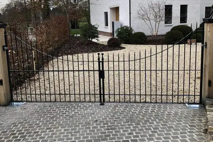 Black steel swing gates across a cobbled drive in front of a white house, Ludlow