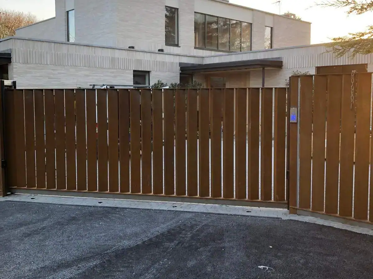 Timber-clad sliding gate closed across a new drive in front of a modern stone house