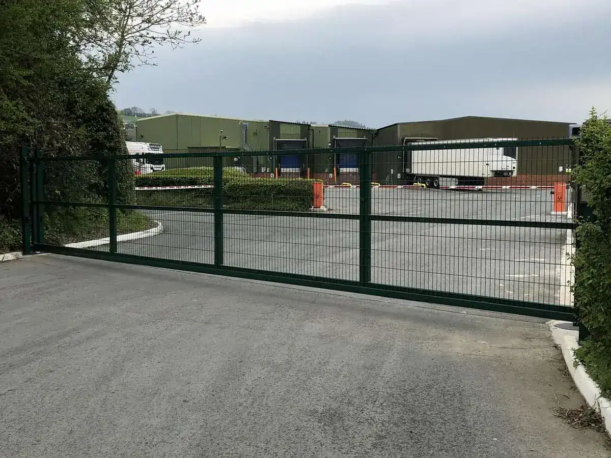 Green steel mesh sliding gate across the road into an industrial estate