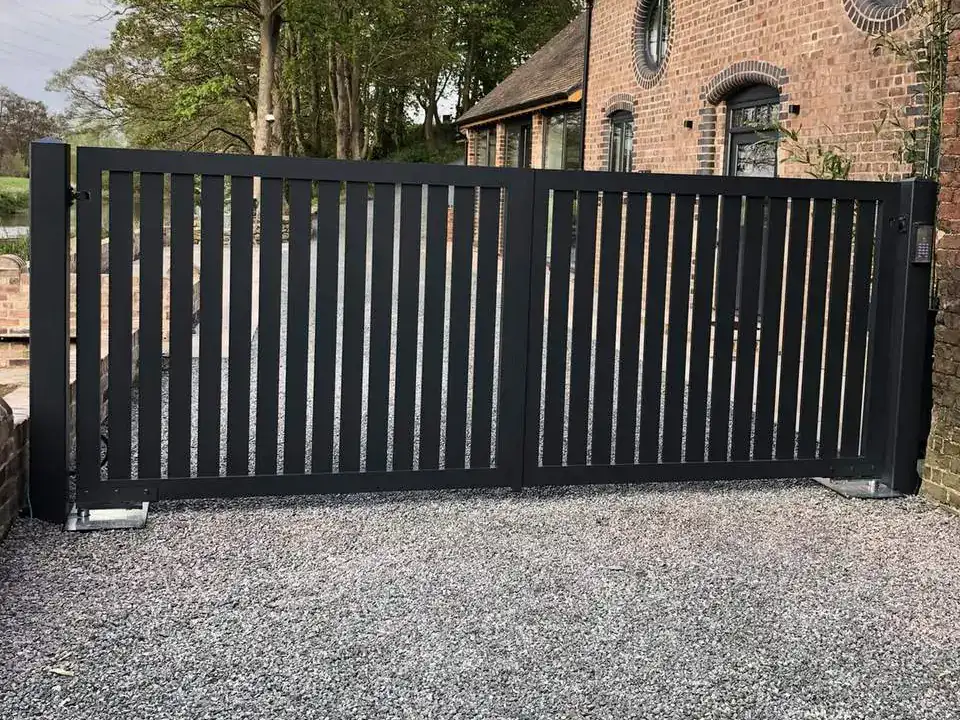 Black slatted double gates across a gravel drive in front of a brick barn conversion