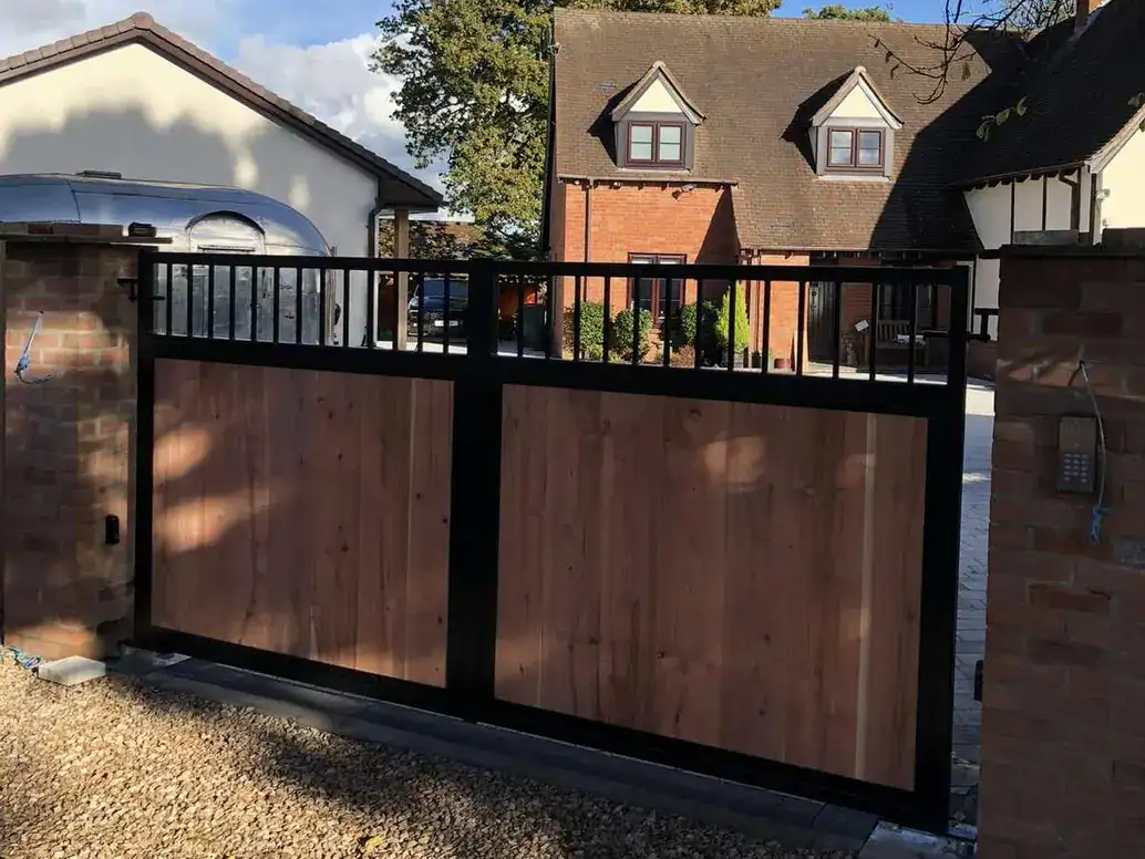 Black-framed timber double gates between brick piers, a house behind