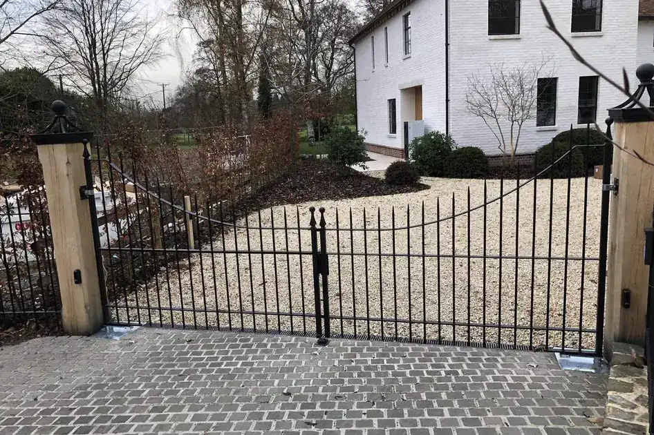 Black iron driveway gates on oak posts across a cobbled drive, white house behind