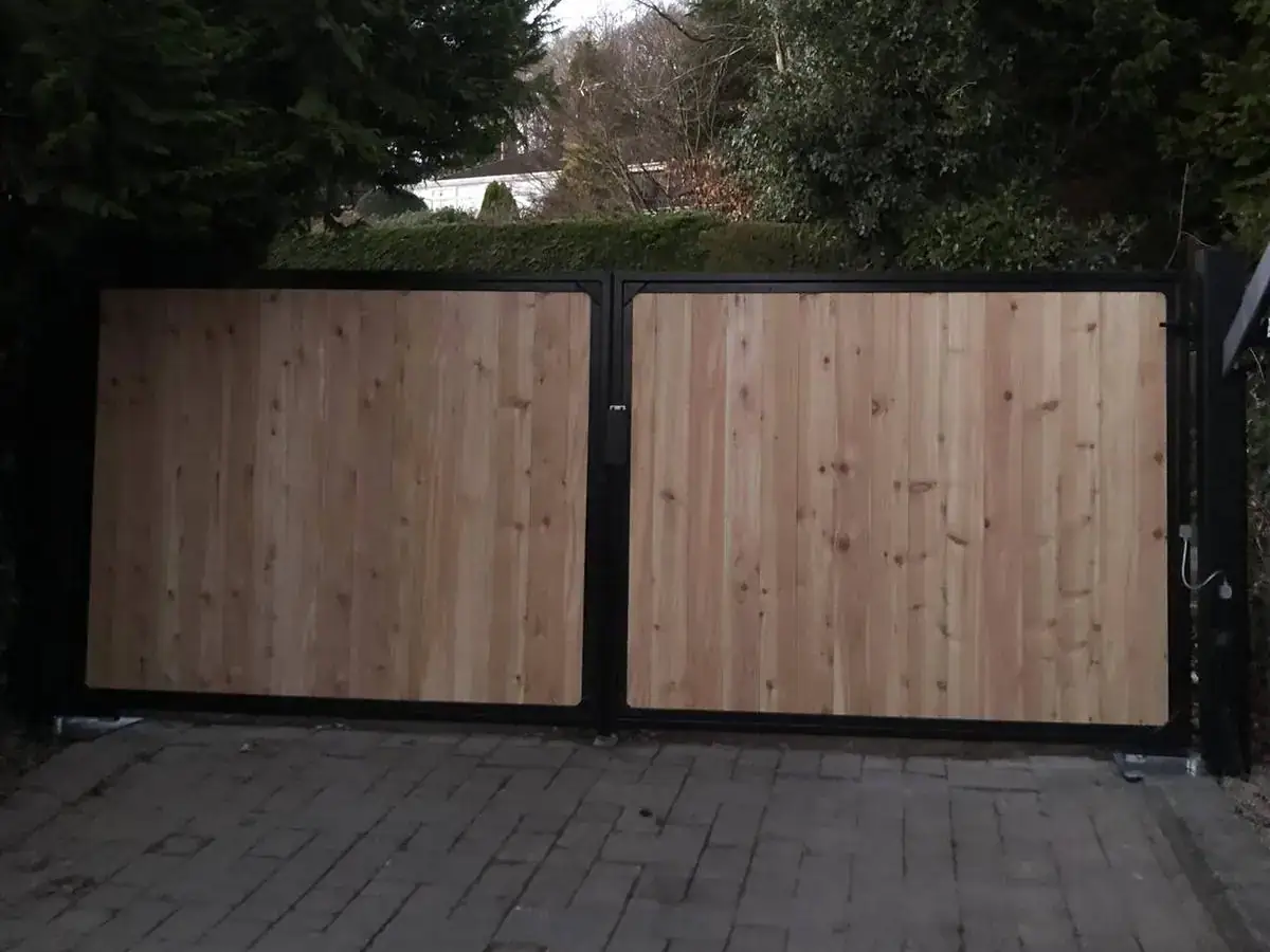 Timber-boarded double gates in a black steel frame across a block-paved drive