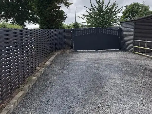 Dark grey woven steel fencing down both sides of a gravel drive to matching arched double gates