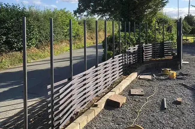 Woven steel fence part built along a lane, the bars woven up to half the height of the posts