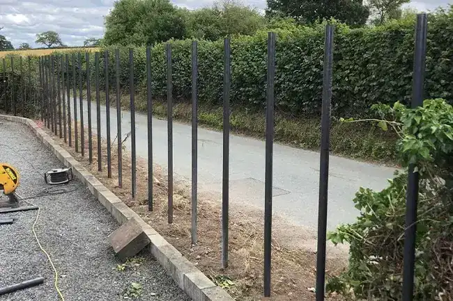 A line of steel fence posts set along a lane in front of a hedge