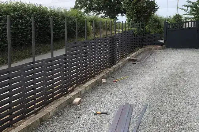 Woven steel fence along a drive with the matching gates at the far end, spare bars on the gravel