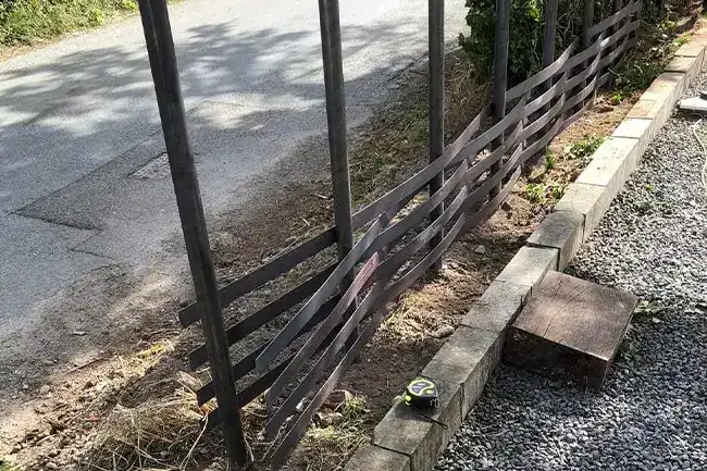 Close up of flat steel bars woven between two fence posts at ground level