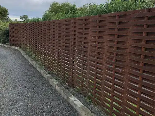 Tall rust brown woven steel fence running the length of a gravel drive