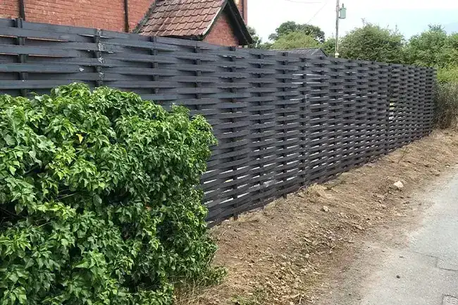 Dark grey woven steel fence running past a brick house, a large ivy bush in front