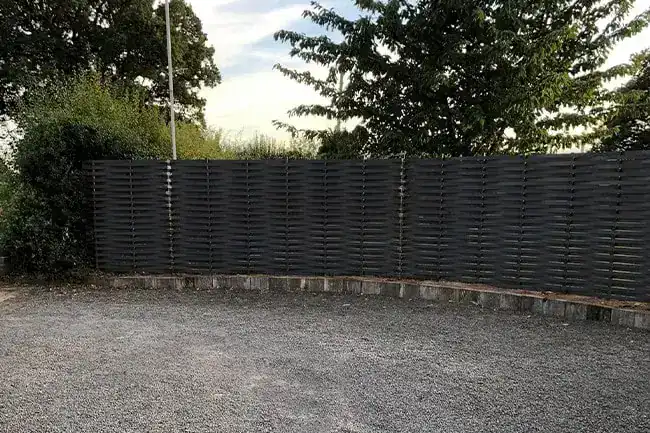 Dark grey woven steel fence along the far edge of a gravel turning area