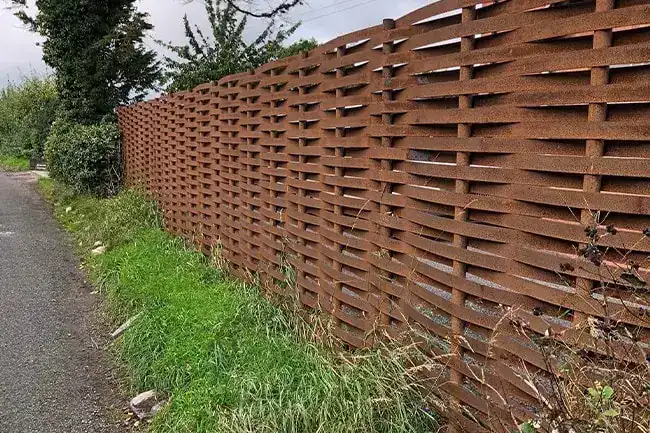 Rust brown woven steel fence along a grass verge beside a narrow path