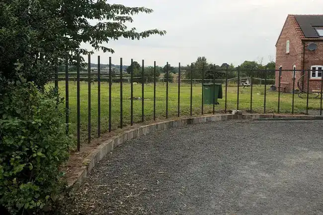Steel fence posts set in a kerbed edge curving around a gravel area, a field beyond