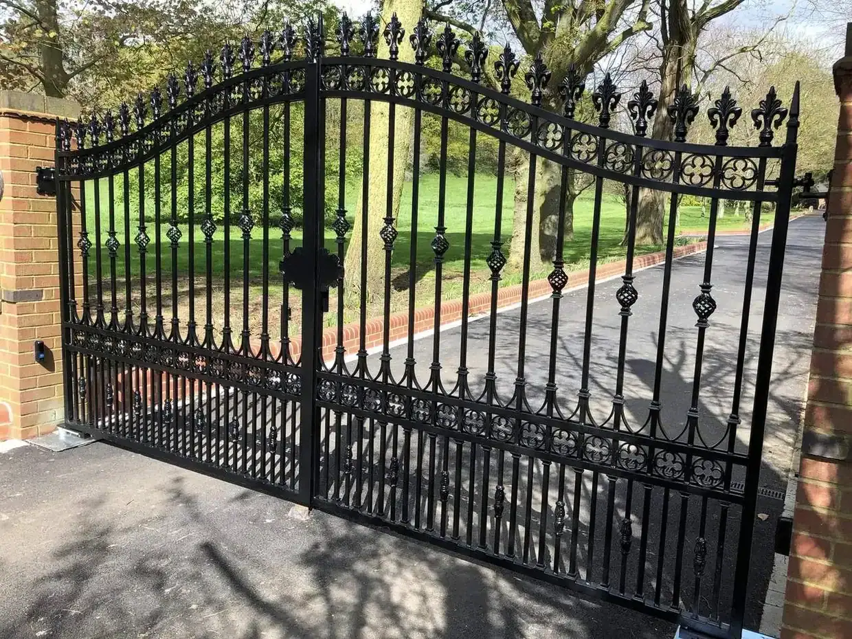 Ornate black iron gates with finials and scrollwork, brick pier and parkland behind