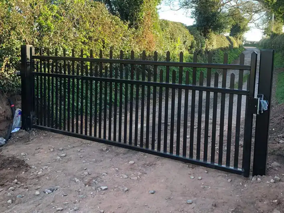 Black iron double gates with vertical bars across a lane between hedges