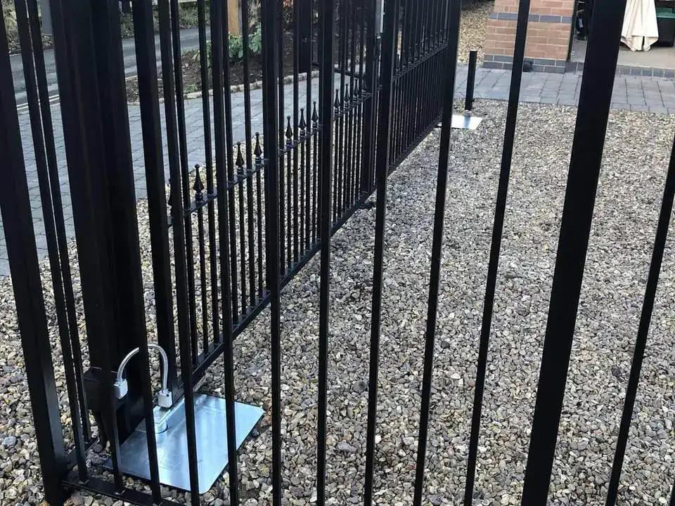 Black iron gate hung on a steel post set into a gravel drive